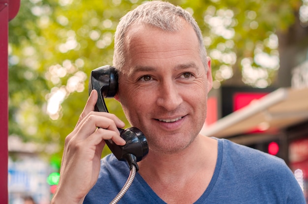 Przystojny mężczyzna dojrzałym rozmawia przez telefon w budce telefonicznej