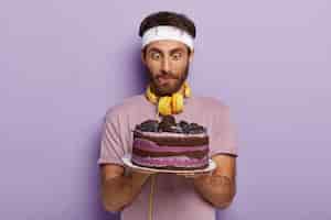 Bezpłatne zdjęcie przystojny mężczyzna niespodziewanie wpatruje się w duży, smaczny tort, oblizuje usta, ma silną ochotę na deser
