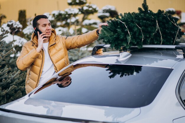 Przystojny mężczyzna opowiada na telefonie samochodem z choinką na wierzchołku