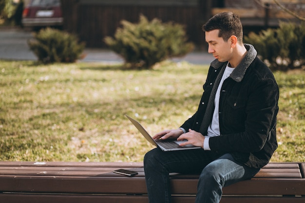 Przystojny mężczyzna siedzi na ławce za pomocą laptopa w parku