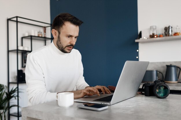 przystojny mężczyzna używający laptopa w domu w kuchni