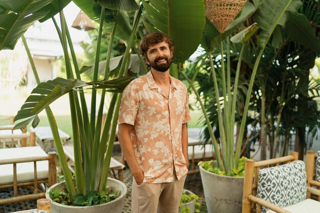 Przystojny mężczyzna z brodą pozuje w kawiarni z tropikalnym wnętrzem