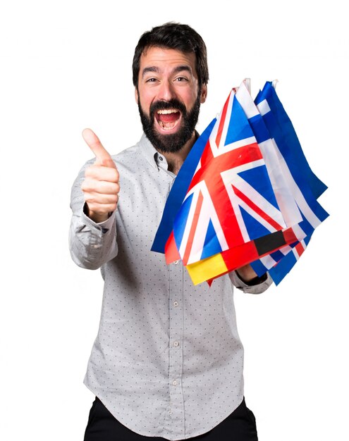 Przystojny mężczyzna z brodą trzyma wiele flag i z kciukiem do góry