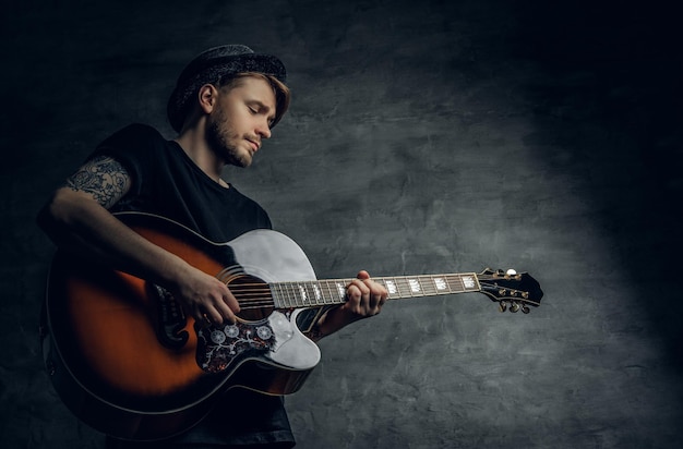 Przystojny młody gitarzysta bluesowy na gitarze akustycznej z tatuażami na ramionach, wykonujący swoje umiejętności muzyczne.