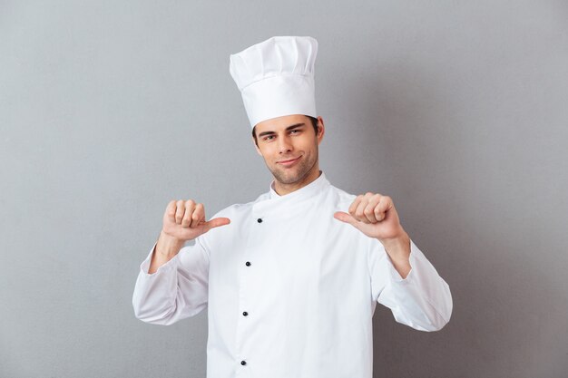 Przystojny młody kucharz w mundurze, wskazując na siebie.