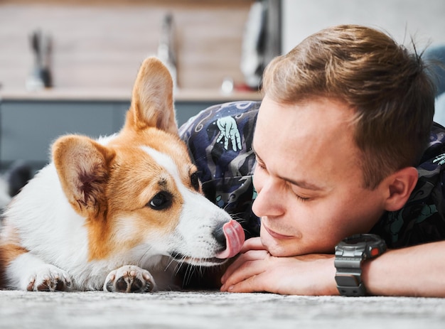 Przystojny młody mężczyzna leżący na podłodze z uroczym psem Corgi