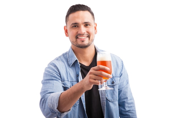 Przystojny młody mężczyzna pijący piwo ze szklanki i uśmiechający się na białym tle