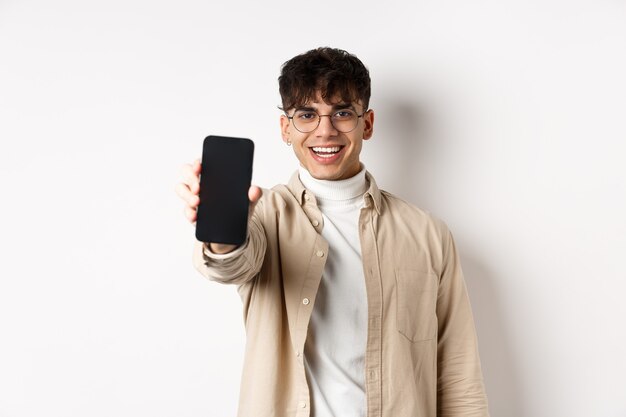 Przystojny młody mężczyzna pokazuje pusty ekran smartfona, stojąc na białym tle. Skopiuj miejsce