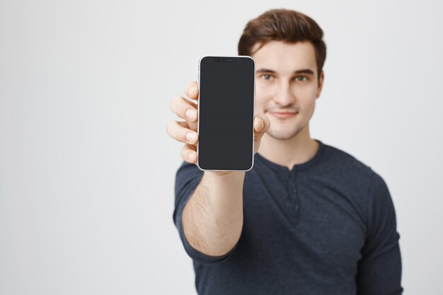 Przystojny młody mężczyzna pokazuje wyświetlacz telefonu komórkowego