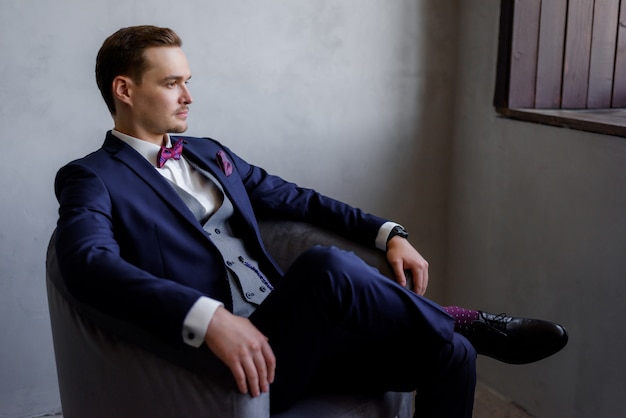 Przystojny młody mężczyzna siedzi w fotelu w pokoju, ubrany w modny garnitur