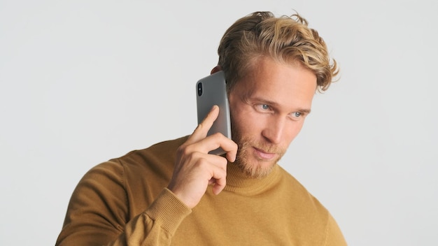 Bezpłatne zdjęcie przystojny stylowy blond brodaty mężczyzna rozmawiający na smartfonie ma ważną rozmowę biznesową na białym tle