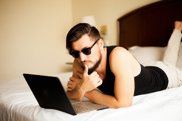 Przystojny stylowy mężczyzna pozowanie na zewnątrz w hotelu, leżąc na łóżku