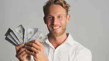 Bezpłatne zdjęcie przystojny uśmiechnięty blond brodaty biznesmen wyglądający szczęśliwie pozujący z pieniędzmi w aparacie na białym tle