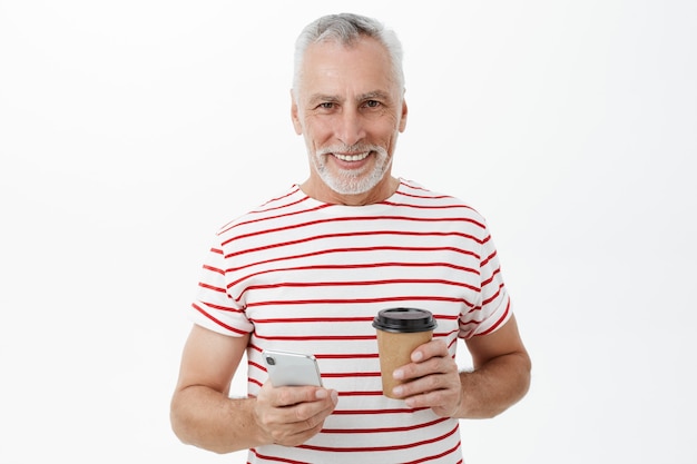 Przystojny uśmiechnięty dojrzały mężczyzna z kawą za pomocą telefonu komórkowego