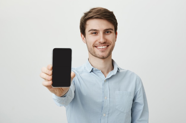 Przystojny, uśmiechnięty mężczyzna pokazuje ekran smartfona