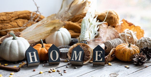Przytulna jesienna kompozycja z ozdobnym słowem home, świecami, dyniami, kukurydzą na drewnianej powierzchni w stylu rustykalnym.