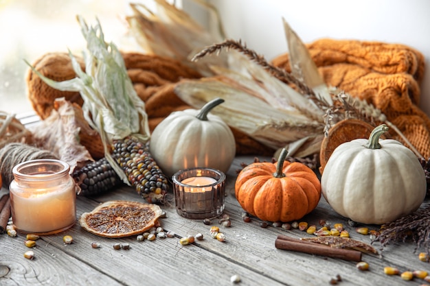 Przytulna jesienna kompozycja ze świecami, dyniami, kukurydzą na drewnianej powierzchni w stylu rustykalnym.
