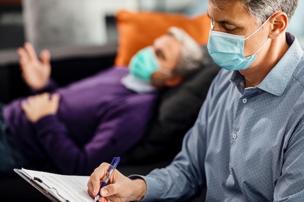 Psychiatra robi notatki podczas doradzania pacjentowi podczas pandemii koronawirusa