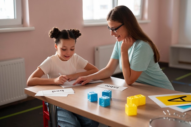 Bezpłatne zdjęcie psycholog pomaga małej dziewczynce w terapii mowy w pomieszczeniu