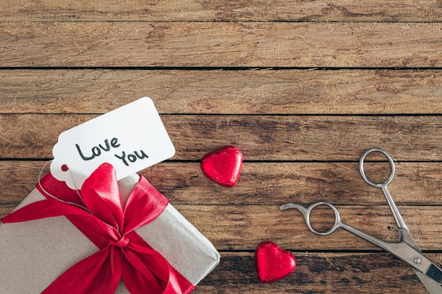 Pudełko na prezent z miłością, etykietą prezentową i cukierkami w kształcie serca na drewnianym tle