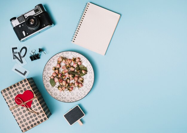 Pudełko z ornamentem serca, aparat fotograficzny, notatnik i kwiaty na talerzu