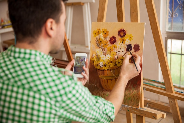 Bezpłatne zdjęcie punkt widzenia mężczyzny kopiującego obraz ze swojego smartfona do własnego obrazu na zajęcia plastyczne