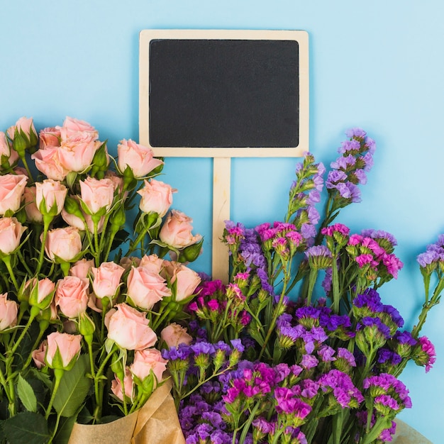 Bezpłatne zdjęcie pusta blackboard etykietka wśrodku kwiatu bukieta przeciw błękitnemu tłu