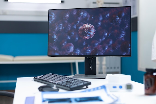 Puste biuro szpitalne z komputerem stojącym na stole z komórką wirusa na ekranie podczas globalnej pandemii koronawirusa. Sala egzaminacyjna wyposażona w profesjonalne narzędzia. Koncepcja medycyny