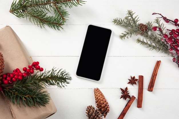 Pusty pusty ekran smartfona na białej drewnianej ścianie z kolorową dekoracją świąteczną i prezentami.