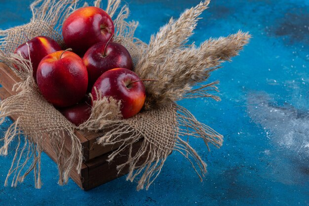 Pyszne czerwone, błyszczące jabłka umieszczone w drewnianym pudełku.