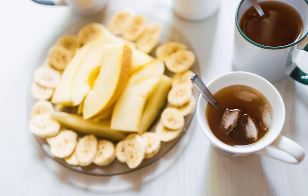 Pyszne pożywne śniadanie z kawą i herbatą, pokrojone na kawałki melon i banan, świeże tosty z masłem i orzechami czekają na stole czekając na towarzystwo lub rodzinę w przytulnej domowej kuchni rano