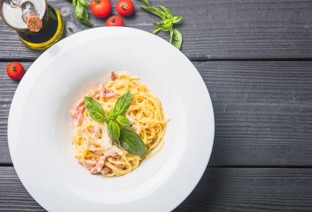 Pyszne spaghetti w białej płytce z oliwą z oliwek; pomidory i liście bazylii na drewnianym stole