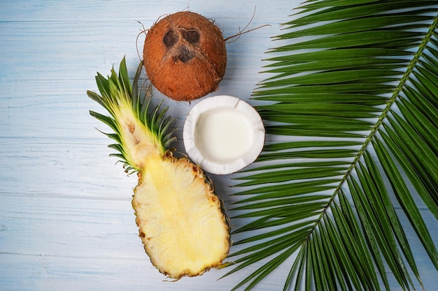 Pyszny pokrojony ananas i świeże orzechy kokosowe z liściem palmowym na białym drewnianym stole