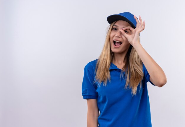 Radosna młoda dziewczyna dostawy ubrana w niebieski mundur i czapkę pokazującą gest wygląd na białym tle na białej ścianie z miejsca na kopię