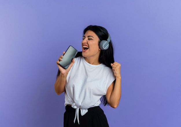 Radosna młoda kaukaska kobieta na słuchawkach trzyma telefon udając, że śpiewa