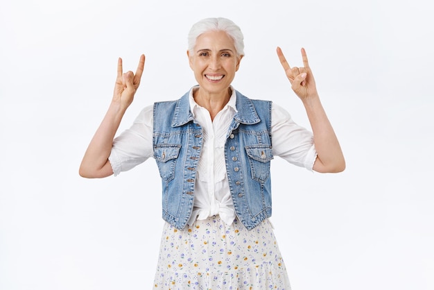 Bezpłatne zdjęcie radosna nowoczesna stylowa fajna babcia bawi się z wnukami słuchając muzyki rocknrollowej opowiadającej stare dobre czasy na koncertach heavy metalowych pokazując rockowe znaki i uśmiechając się beztrosko białe tło