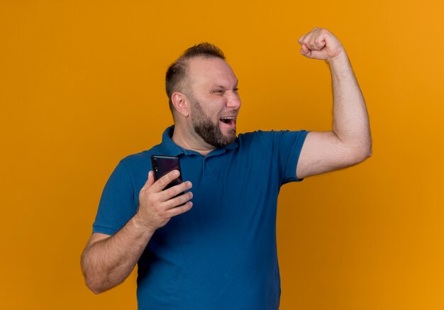 Radosny dorosły słowiański mężczyzna trzyma telefon komórkowy, patrząc na bok, robi tak gest