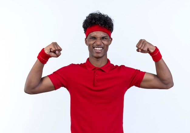 Radosny młody afro-amerykański sportowy mężczyzna nosi pałąk i opaskę robi silny gest na białym tle