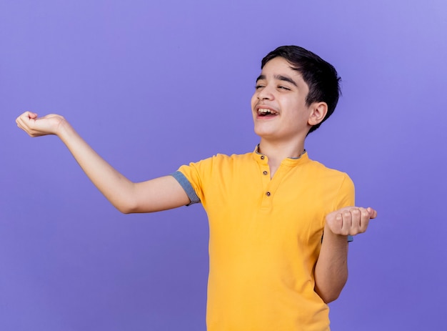 Radosny młody chłopak patrząc na bok wyciągając ręce na białym tle na fioletowej ścianie