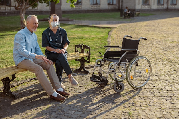 Radosny starzejący się pacjent płci męskiej spędzający czas na świeżym powietrzu z pielęgniarką opiekuńczą na sobie
