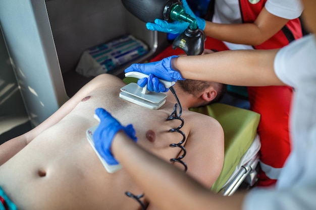 Bezpłatne zdjęcie ratownicy medyczni udzielają pomocy medycznej rannemu pacjentowi w drodze do szpitala asystenci pogotowia ratunkowego zakładają nieinwazyjną maskę wentylacyjną w karetce pogotowia