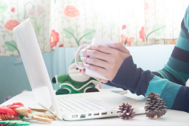 Ręce gospodarstwa filiżankę kawy i przy użyciu komputera przenośnego z dekoracji Christmas, Zakupy online