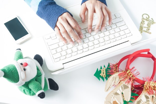 Ręce kobiety wpisując na klawiaturze laptopa, używając smartphone z dekoracją świąteczną, zakupy online