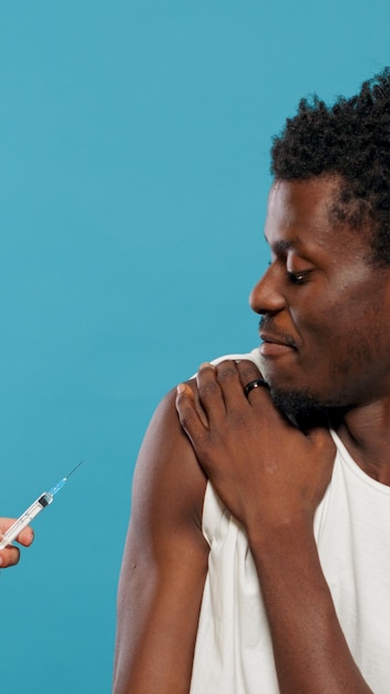 Ręce lekarza przygotowującego się do zaszczepienia młodego człowieka przeciwko koronawirusowi. Portret osoby obawiającej się zastrzyku szczepionki i strzykawki z igłą, pozostawiając miejsce na szczepienie. Przestraszony dorosły