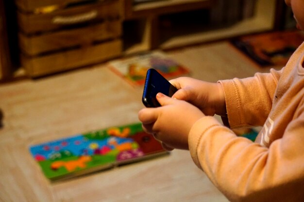Ręce małego chłopca bawiącego się smartfonem zamiast swoimi zabawkami (zabawki i podkłady)