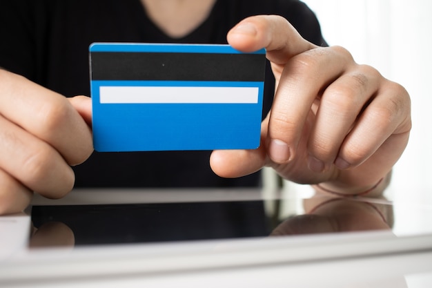 Ręce osoby trzymającej niebieską kartę kredytową na odbijającej powierzchni w białym pokoju