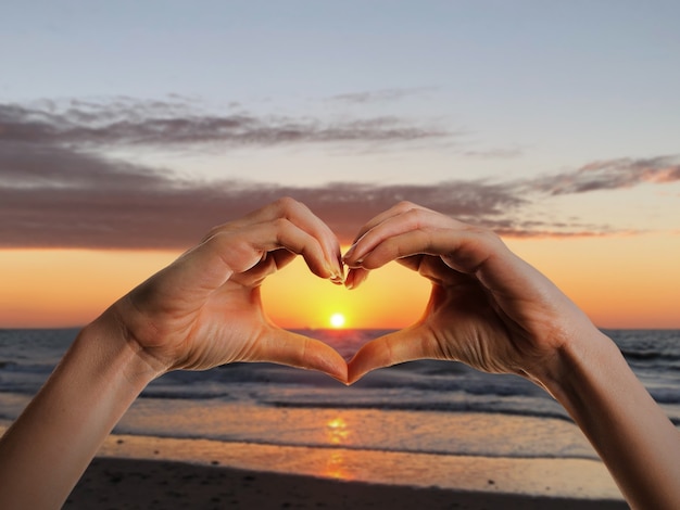 Bezpłatne zdjęcie ręce w kształcie serca na zachodzie słońca
