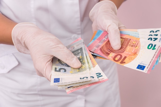 Ręce w rękawiczkach medycznych z banknotami euro