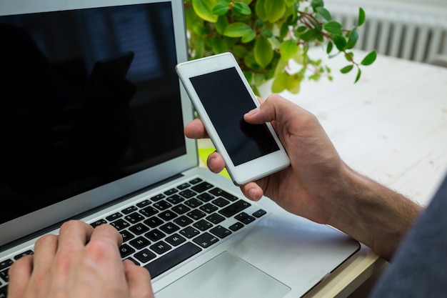 Ręce wykonawczej męskiej za pomocą telefonu komórkowego i laptopa