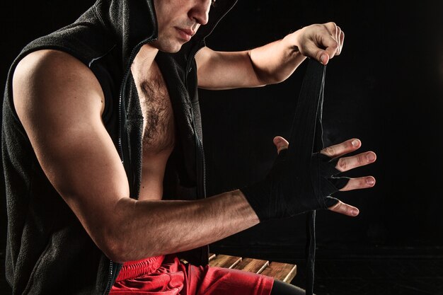 Ręce z bandażem muskularnego mężczyzny trenującego kickboxing na czarno